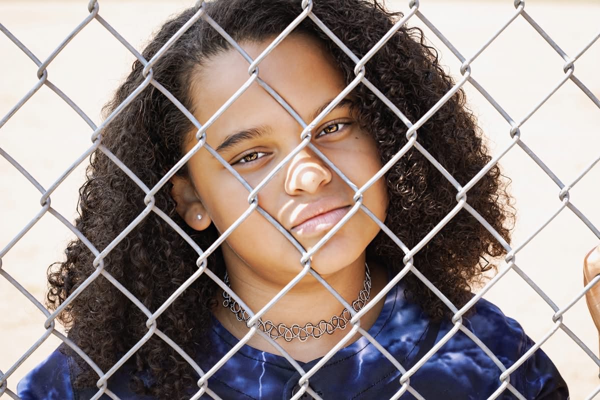 Young athlete smiling at the ball field fence